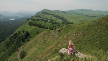 Genç bir kız turist dağın kenarına gelir ve ellerini kaldırır. Yeşil dağların güzel manzarasının tadını çıkarırlar..