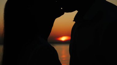 Birbirlerine aşık çiftlerin yakın çekim silueti, erkek ve kadın, tropik adada gün batımında öpüşüyorlar. Adada yeni evlilerin balayı.