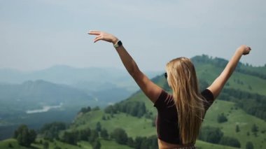 Genç bir kadın gün batımına karşı ellerini kaldırıp sıcak bir yaz akşamının tadını çıkarıyor. Mutlu bir kız turist bir dağa tırmanma başarısı ile sevinir..
