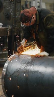 Metal fabrikasında çalışan bir işçi metali işliyor. Öğütücüden kıvılcımlar çıkıyor. Metal inşaat fabrikası. Dikey video.