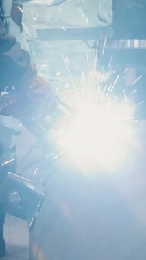  Fabrikada çalışan bir işçi metal bir yapıya kaynak yapar. Metal yapılar üreten bir fabrika. Kaynak metalinden kıvılcımlar. Endüstriyel üretim. Dikey video.