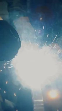  Fabrikada çalışan bir işçi metal bir yapıya kaynak yapar. Metal yapılar üreten bir fabrika. Kaynak metalinden kıvılcımlar. Endüstriyel üretim. Dikey video.