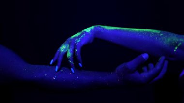 Bir adam ve kadının elleri neon ışıkta parlayan boyalarla boyanmış. Eller birbirine dokunur..