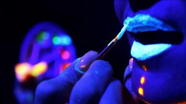 Kızların dudaklarını neon ışığın altında parlayan boyayla boyayın. Floresan makyaj..