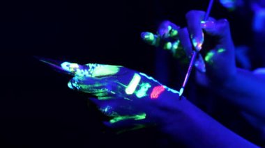 Bir kadının eline fırçayla parlayan boya sürerken yakın plan fotoğrafı. Floresan makyaj..