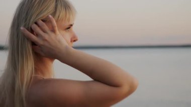 Genç sarışın bir kızın portresi akşam denizin arka planına karşı. Kız okyanus kıyısındaki kameraya poz veriyor..