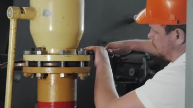 Fabrikada güvenlik kaskı takan bir işçi büyük bir ingiliz anahtarıyla fındığı sıkıyor. İngiliz anahtarı fındığı sıkıyor. Bir işçi boru hattını tamir ediyor.