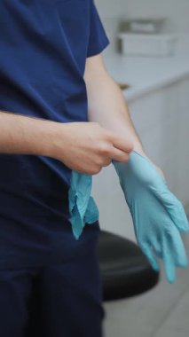 Klinikteki bir hastayı görmeden önce doktorların elleri mavi koruyucu eldiven takıyor. Dikey video.