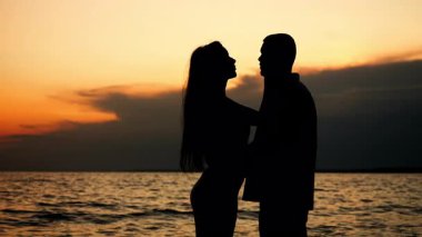 Birbirini seven iki insanın silueti. Bir adam ve bir kadın. Tropik bir adanın kıyısında durup birbirlerini öpüyorlar. Tropik bir plajda aile tatili..