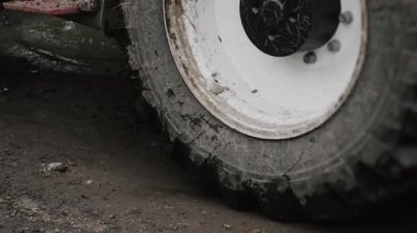 A close-up of a tractors wheels with a bucket driving through mud and puddles at a construction site. Heavy equipment used for construction and excavation work.