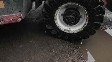 A close-up of a tractors wheels with a bucket driving through mud and puddles at a construction site. Heavy equipment used for construction and excavation work.