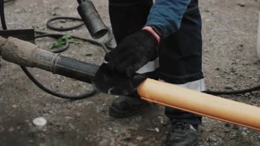 A worker insulates a joint between two plastic pipes. An engineer heats bitumen pipe insulation with a gas torch. Laying plastic gas pipes underground.