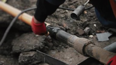 A worker insulates a joint between two plastic pipes. An engineer heats bitumen pipe insulation with a gas torch. Laying plastic gas pipes underground.