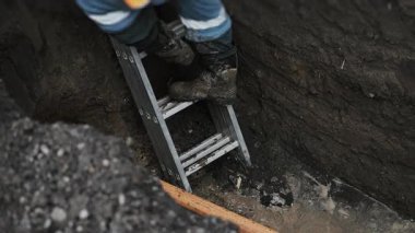 A drilling rig worker descends a ladder into a pit and checks the connection between the drill and the gas pipe. Laying plastic gas pipes underground.