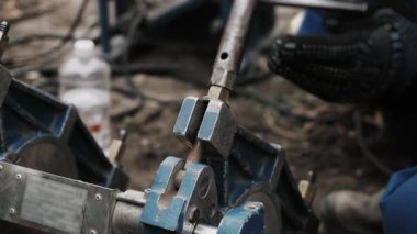 Close-up of a workers gloved hands tightening a pipe welding machine fastener with a wrench.
