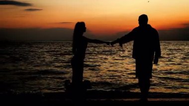 A silhouette of a young couple on their honeymoon standing on the seashore, hugging and holding hands. Family vacation on a tropical island.