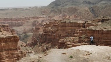 A male tourist stands on the edge of a mountain cliff and takes pictures of the canyon landscape on his phone. Mountain tourism.