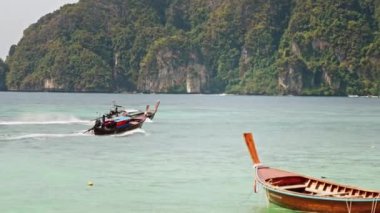 Ön planda uzun bir kuyruk botu, arka planda diğer tekneler geçiyor..