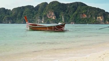 Suda tek bir Tayland teknesi var, insan yok, arkada dağ var.