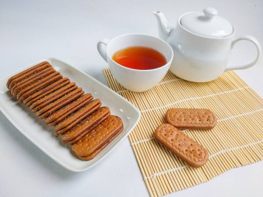 Bir grup çikolatalı sandviç bisküvisi ve beyaz arka planda bir fincan çay.