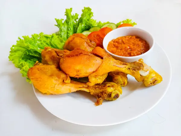 stock image Pecel Ayam is traditional Indonesian fried chicken (drumsticks) with fresh vegetable and chili sauce (sambal tomat), served in white plate