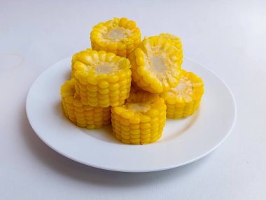 Tatlı mısır koçanları beyaz tabakta yarıya iniyor. 