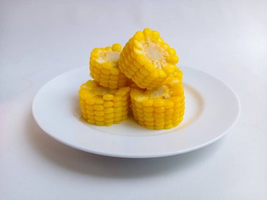 Tatlı mısır koçanları beyaz tabakta yarıya iniyor. 