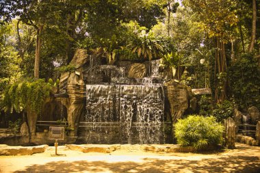 Şelale, canlı yeşillik ve yemyeşil bitkilerle çevrili Taman Rimba Melaka, Malezya 'daki doğal kayaların üzerinden zarif bir şekilde akar ve ormanda barışçıl bir atmosfer yaratır..