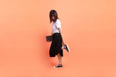 Tayland üniversitesi üniformalı neşeli bir bayan öğrenci. Elinde turuncu arka planda izole edilmiş bir ders kitabı var. Uluslararası Öğrenciler Günü, Dünya Öğrenciler Günü. Gen Z