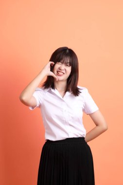 Tayland üniversitesi üniformalı neşeli bir bayan öğrenci. Turuncu arka planda birden fazla poz veriyor. Uluslararası Öğrenciler Günü, Dünya Öğrenciler Günü. Gen Z