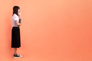 Tayland üniversitesi üniformalı neşeli bir bayan öğrenci. Elinde turuncu arka planda izole edilmiş bir ders kitabı var. Uluslararası Öğrenciler Günü, Dünya Öğrenciler Günü. Gen Z