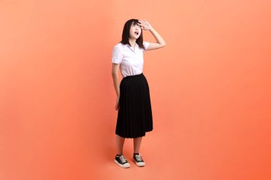 Tayland üniversitesi üniformalı neşeli bayan öğrenci turuncu arka planda izole edilmiş gibi görünüyor. Uluslararası Öğrenciler Günü, Dünya Öğrenciler Günü. Gen Z