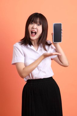 Tayland Üniversitesi üniformalı neşeli bayan öğrenci portakal rengi arka planda izole edilmiş cep telefonunu tutuyor. Uluslararası Öğrenciler Günü, Dünya Öğrenciler Günü. Gen Z