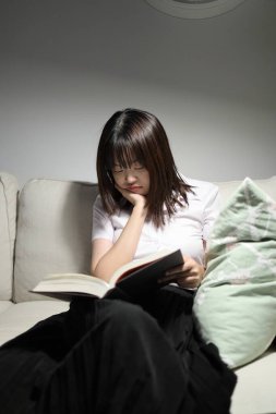 Tayland üniversitesi üniformalı genç bir kız öğrenci oturma odasında bir kanepede oturup kitap okuyor. Uluslararası Öğrenciler Günü, Dünya Öğrenciler Günü. Gen Z