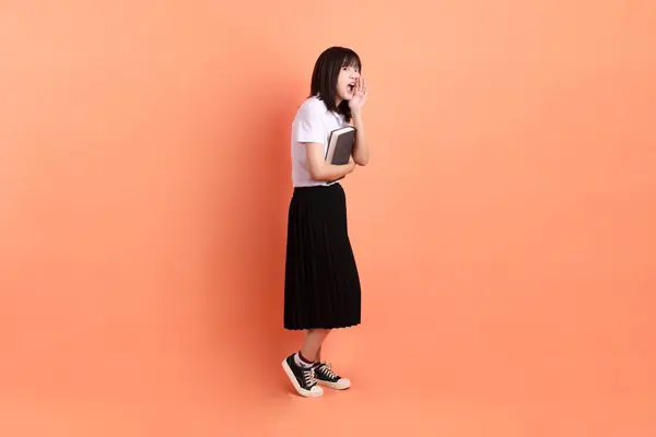 stock image Cheerful female student in Thai university uniform with gesture of holding a textbook isolated on orange background. International Students' Day, World Students' Day.