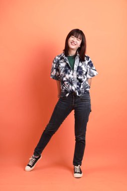 Mutlu SONGKRAN GÜNÜ. Turuncu arka planda izole edilmiş poz veren yaz kıyafetleri içinde neşeli, sevimli, genç Asyalı bir kadın. Tayland Yeni Yıl Günü.