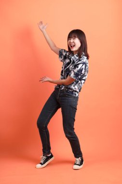 Mutlu SONGKRAN GÜNÜ. Turuncu arka planda izole edilmiş bir şekilde işaret eden yaz kıyafetleri içinde neşeli, sevimli, genç Asyalı kadın. Tayland Yeni Yıl Günü.