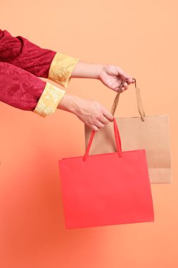 Yeni Çin yılın kutlu olsun. Turuncu arka planda kırmızı el çantası taşıyan, geleneksel kırmızı kıyafetler giyen Asyalı son sınıf öğrencisinin eli..