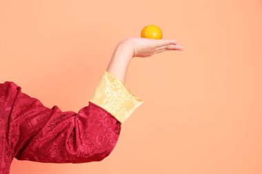 Yeni Çin yılın kutlu olsun. Turuncu arka planda izole edilmiş portakalla el ele tutuşan kırmızı geleneksel kıyafetler giyen Asyalı son sınıf öğrencisinin eli..