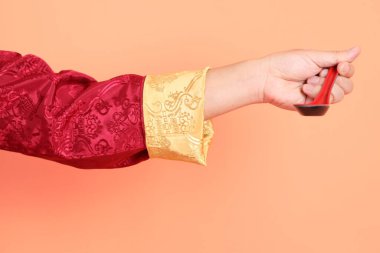 Yeni Çin yılın kutlu olsun. Çinli son sınıf öğrencisinin eli turuncu arka planda izole edilmiş el ele tutuşan kırmızı geleneksel kıyafetler giyiyor..