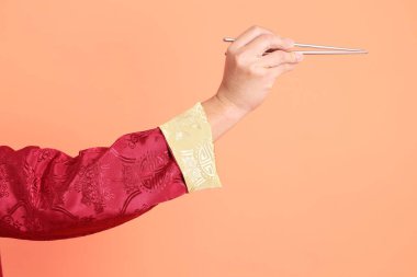 Yeni Çin yılın kutlu olsun. Kırmızı geleneksel cheongsam qipao ya da changshan elbisesi giyen Asyalı son sınıf öğrencisinin eli turuncu arka planda izole edilmiş gümüş çubuklarla el ele tutuşuyor..