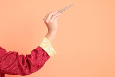 Yeni Çin yılın kutlu olsun. Kırmızı geleneksel cheongsam qipao ya da changshan elbisesi giyen Asyalı son sınıf öğrencisinin eli turuncu arka planda izole edilmiş gümüş çubuklarla el ele tutuşuyor..