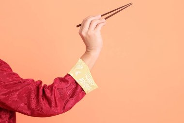 Yeni Çin yılın kutlu olsun. Kırmızı geleneksel cheongsam qipao ya da changshan elbisesi giyen Asyalı son sınıf öğrencisinin eli turuncu arka planda izole edilmiş kahverengi çubukları tutan el hareketleriyle..