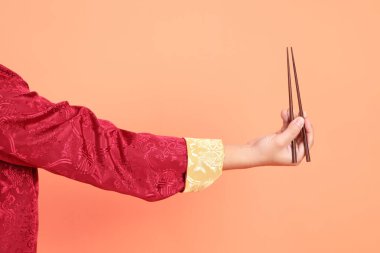 Yeni Çin yılın kutlu olsun. Kırmızı geleneksel cheongsam qipao ya da changshan elbisesi giyen Asyalı son sınıf öğrencisinin eli turuncu arka planda izole edilmiş kahverengi çubukları tutan el hareketleriyle..