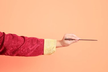 Yeni Çin yılın kutlu olsun. Kırmızı geleneksel cheongsam qipao ya da changshan elbisesi giyen Asyalı son sınıf öğrencisinin eli turuncu arka planda izole edilmiş kahverengi çubukları tutan el hareketleriyle..