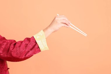 Yeni Çin yılın kutlu olsun. Kırmızı geleneksel cheongsam qipao ya da changshan elbisesi giyen Asyalı son sınıf öğrencisinin eli turuncu arka planda izole edilmiş beyaz çubuklarla el ele tutuşuyor..