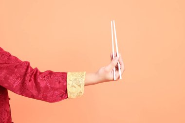 Yeni Çin yılın kutlu olsun. Kırmızı geleneksel cheongsam qipao ya da changshan elbisesi giyen Asyalı son sınıf öğrencisinin eli turuncu arka planda izole edilmiş beyaz çubuklarla el ele tutuşuyor..