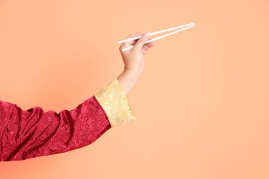 Yeni Çin yılın kutlu olsun. Kırmızı geleneksel cheongsam qipao ya da changshan elbisesi giyen Asyalı son sınıf öğrencisinin eli turuncu arka planda izole edilmiş beyaz çubuklarla el ele tutuşuyor..