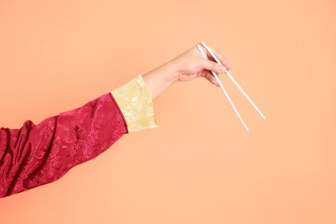 Yeni Çin yılın kutlu olsun. Kırmızı geleneksel cheongsam qipao ya da changshan elbisesi giyen Asyalı son sınıf öğrencisinin eli turuncu arka planda izole edilmiş beyaz çubuklarla el ele tutuşuyor..