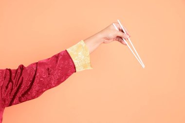 Yeni Çin yılın kutlu olsun. Kırmızı geleneksel cheongsam qipao ya da changshan elbisesi giyen Asyalı son sınıf öğrencisinin eli turuncu arka planda izole edilmiş beyaz çubuklarla el ele tutuşuyor..